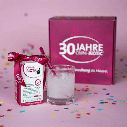 OMNi-BiOTiC 6 mit Glas und Löffel vor der Jubiläumsbox umgeben von Konfetti