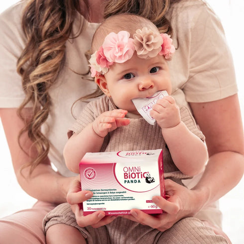 Ein Baby mit einer Packung OMNi-BiOTiC PANDA und einem Sachet im Mund
