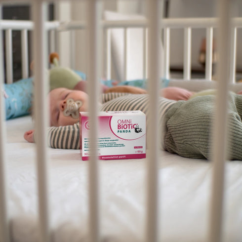 Eine Packung OMNi-BiOTiC PANDA neben einem schlafenden Baby