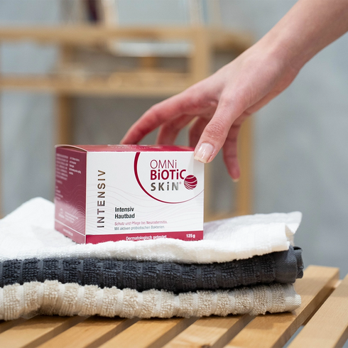 Eine Hand greift nach einer Packung OMNi-BiOTiC SKiN Intensiv-Hautbad