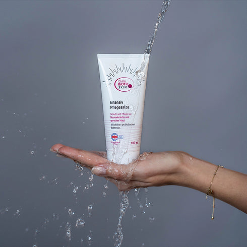 Eine OMNi-BiOTiC SKiN Intensiv-Pflegesalbe unter einem Wasserstrahl