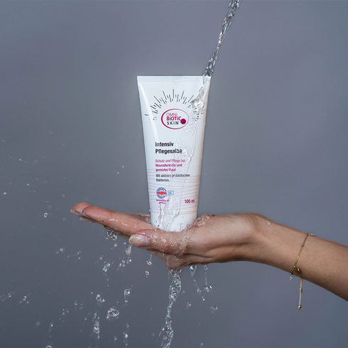 Eine OMNi-BiOTiC SKiN Intensiv-Pflegesalbe unter einem Wasserstrahl